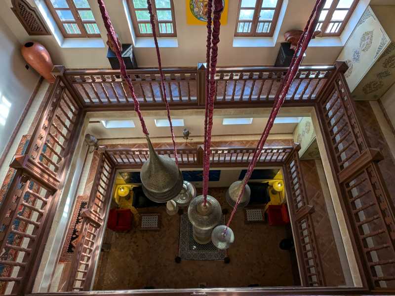 Ornate hanging lanterns and carved wooden balconies inside a restored riad in Essaouira