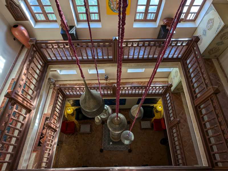 Ornate hanging lanterns and carved wooden balconies inside a restored riad in Essaouira