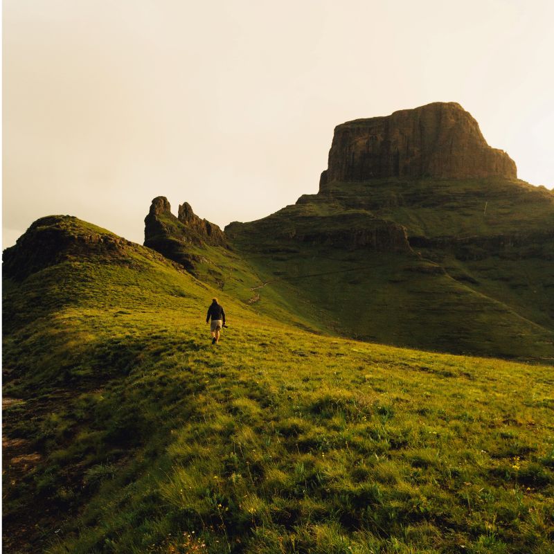 Drakensberg walker crosses grassland beneath a rugged peak, South Africa