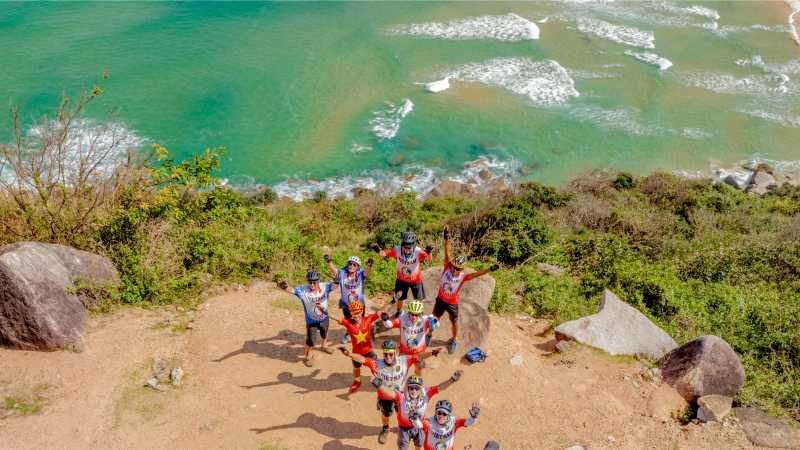Cycling group celebrating on a coastal hillside with sweeping ocean views behind