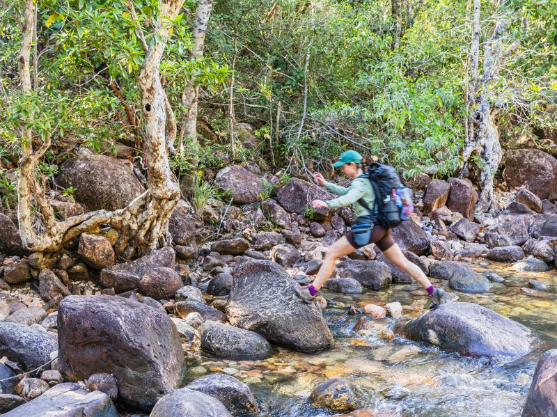 Thorsborne Trail trekker crossing a rocky creek through rainforest, Queensland | Eloise Weston