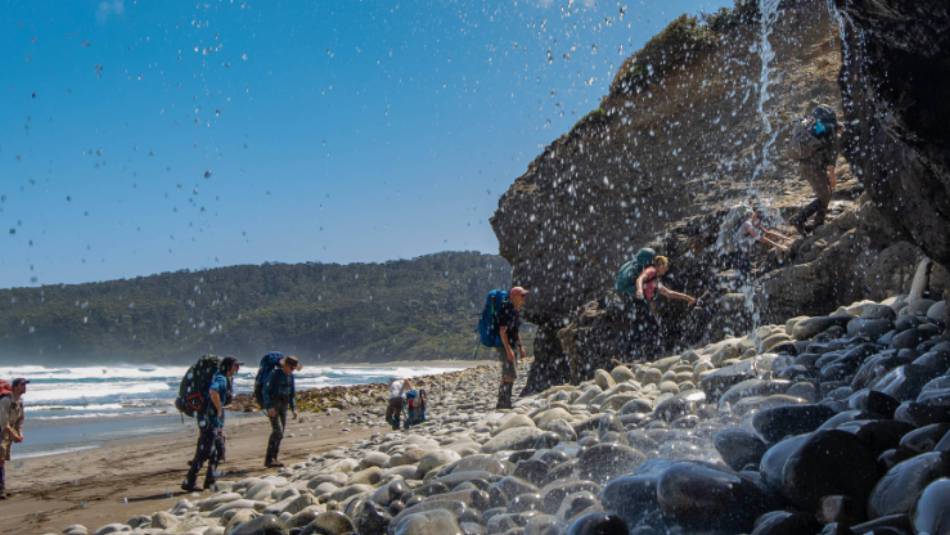 Trekking behind a waterfall on the South Coast Track | John Dalton