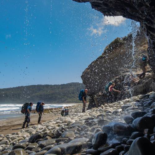 Trekking behind a waterfall on the South Coast Track