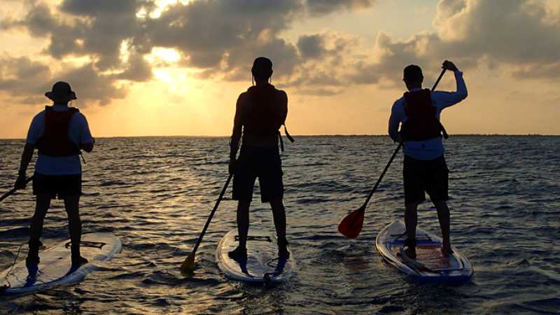 Stand-up paddleboard across the calm waters of Lighthouse Reef Atoll at sunset