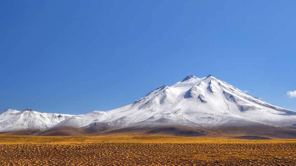 Scattered across the landscape and rising like monoliths through the clouds, multiple volcanos can be spotted looking across the Atacama Desert